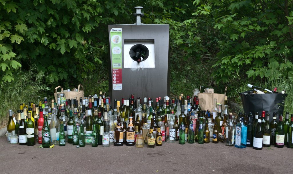 A glass container with lots of glass bottles placed next to the container.