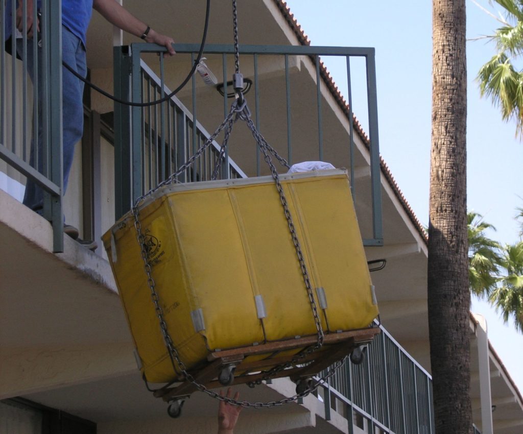 Two guys moving a big yellow laundry basket from one floor to another.