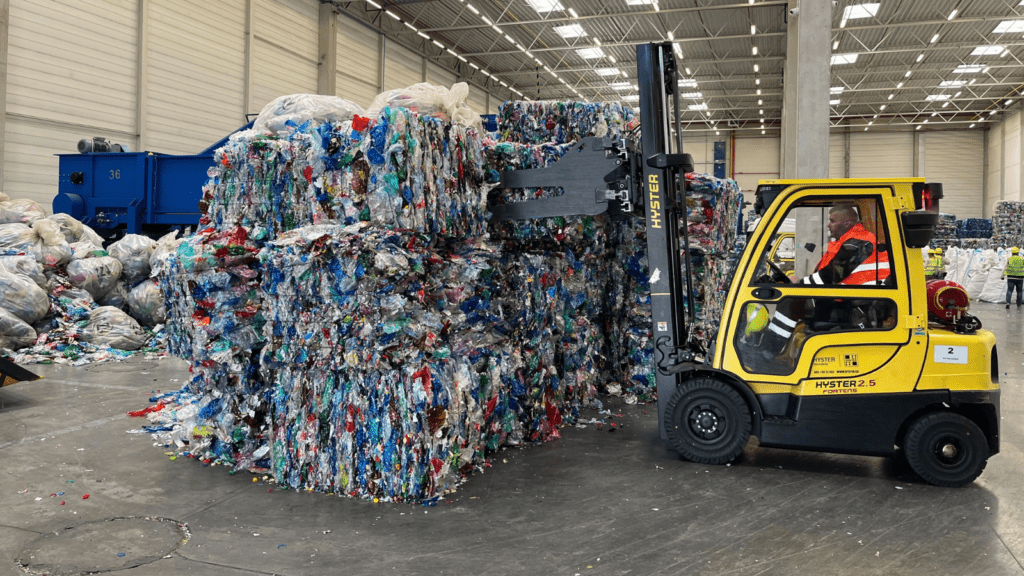 A worker in a forklift truck moving recycled plastic bottles and aluminum cans in recycling facility.