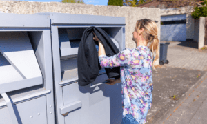 A woman putting used clothes into the container.