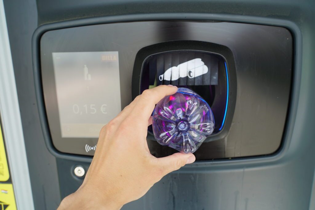 An arm of a man who is putting a plastic bottle into a reverse vending machine.