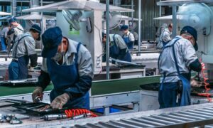 Workers dressed in safety uniforms, using special equipment to work around machines.