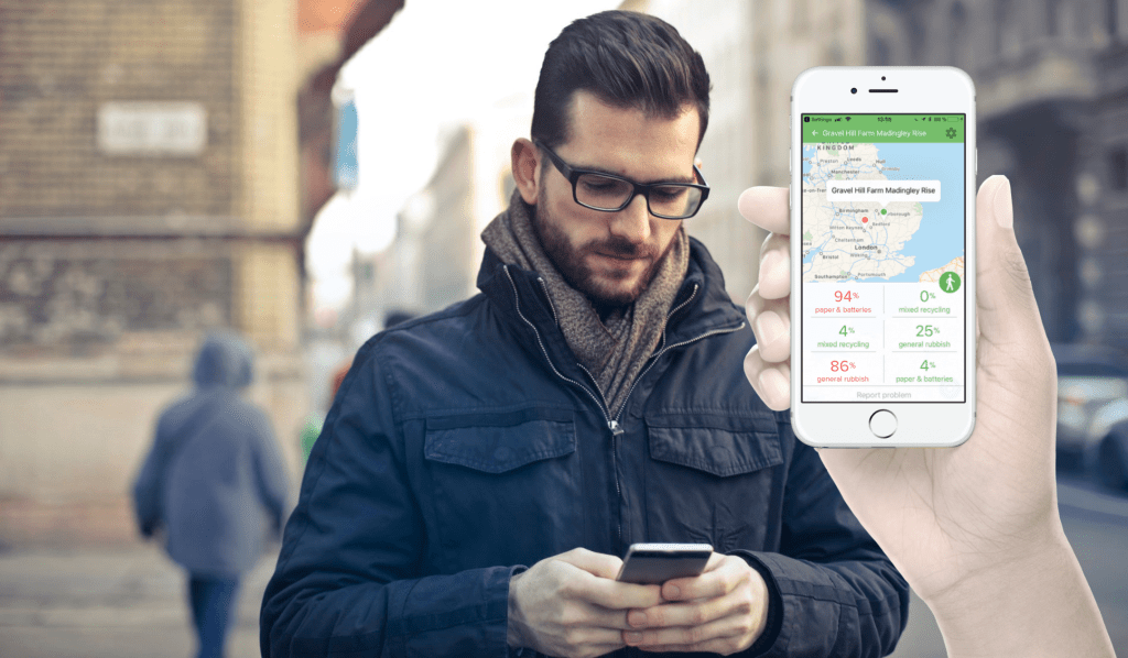 A man holding a phone and standing on the street. A hand holding a phone with our Sensoneo citizen app.